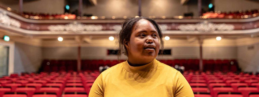 Person in yellow top looking around an empty theatre, will rows of red seats behind.