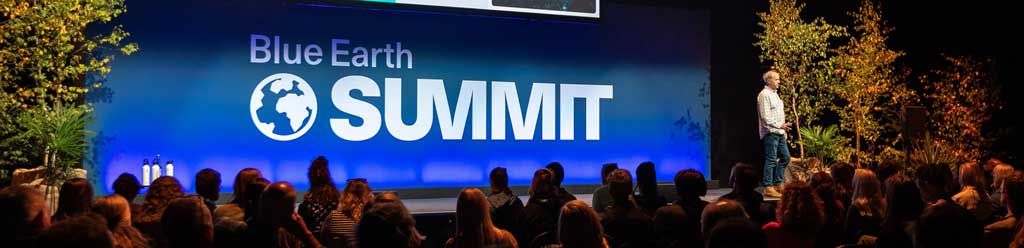 Speaker an audience, with Blue Earth Summit logo on screen behind.