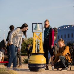 People on a quayside looking at a harbour buoy made into an interactive sound sculpture