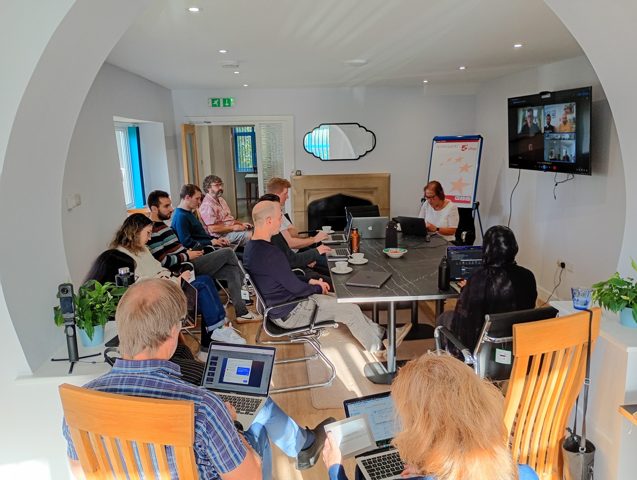 Photo of the Calvium team around a conference table, with other colleagues on a video call shown on the wall mounted TV.