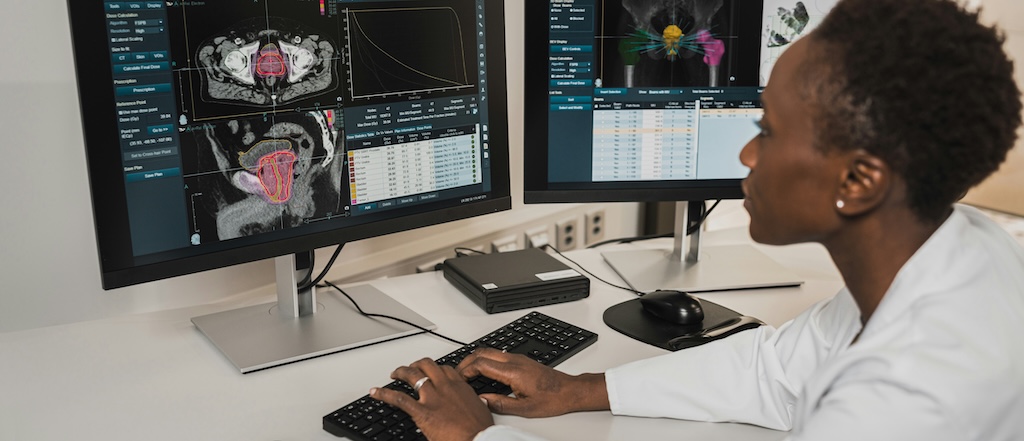 Dr in white coat working at a computer, which is showing organ scans and medical data.
