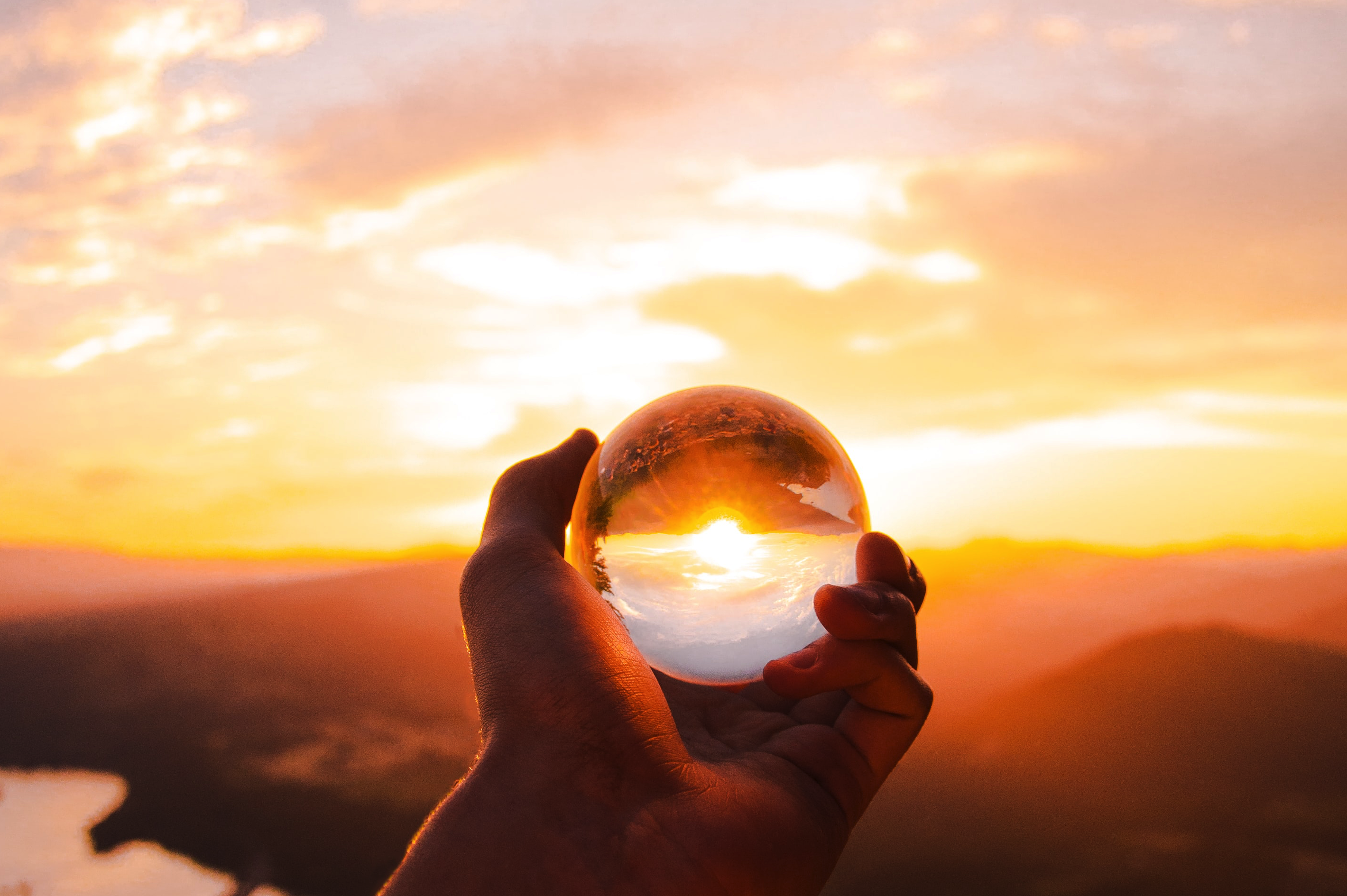 Photo of hand holding crystal ball at sunrise