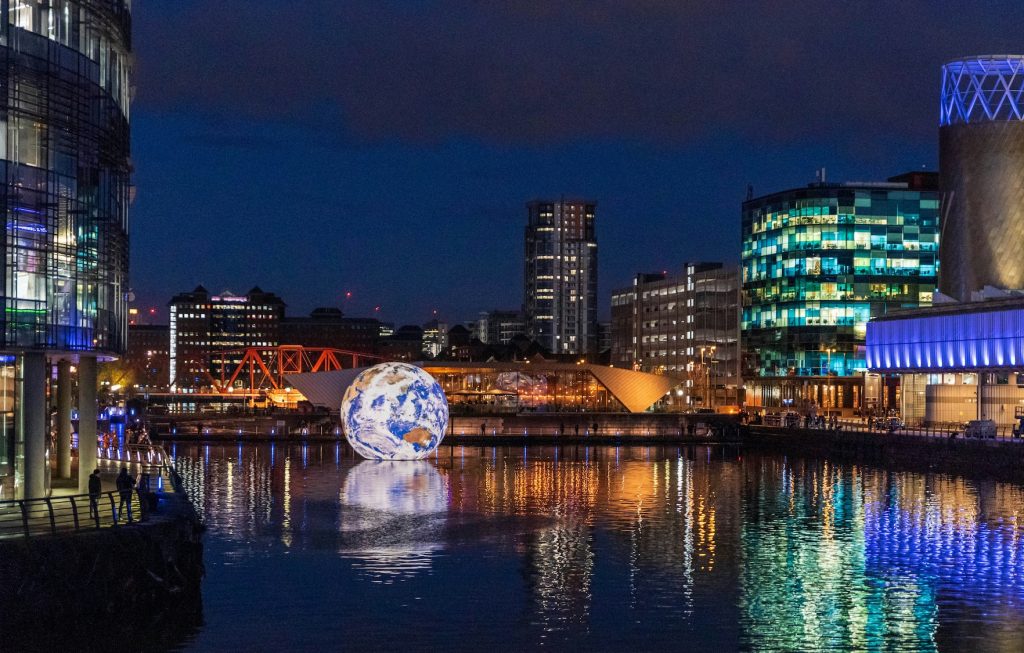 Illuminated globe floating on the water at Salford Quays at night.