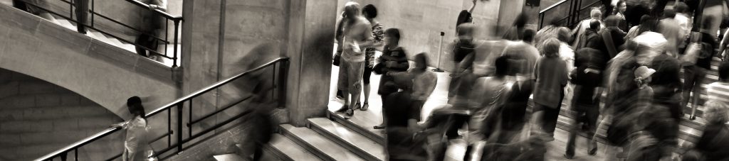 Blurred black and white photo of people walking up and down stairs in a public building.