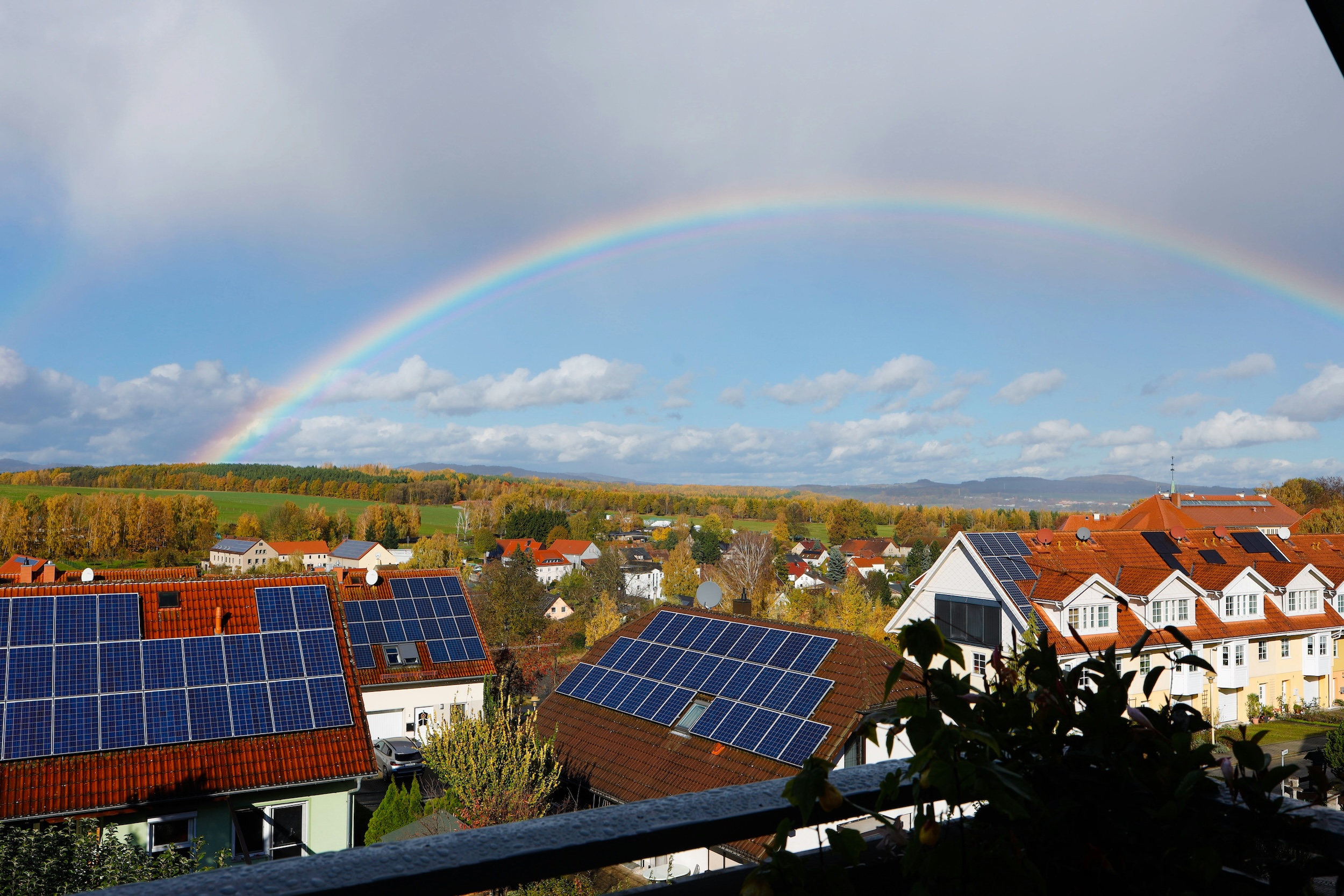 Houses with solar panels with green hills and fields behind, with a rainbow above.