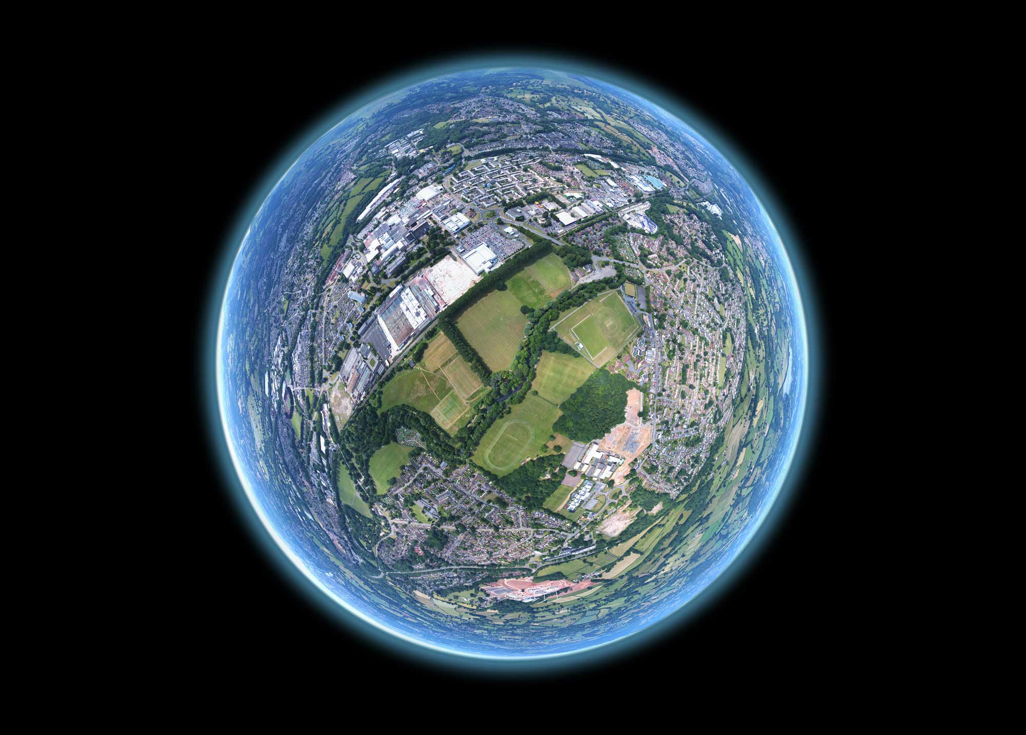 Fish-eye lens view of sports fields and suburbs, which blends to blue as it zooms out to the edges of the circle. The background is black, similar to an image of the Earth in space.
