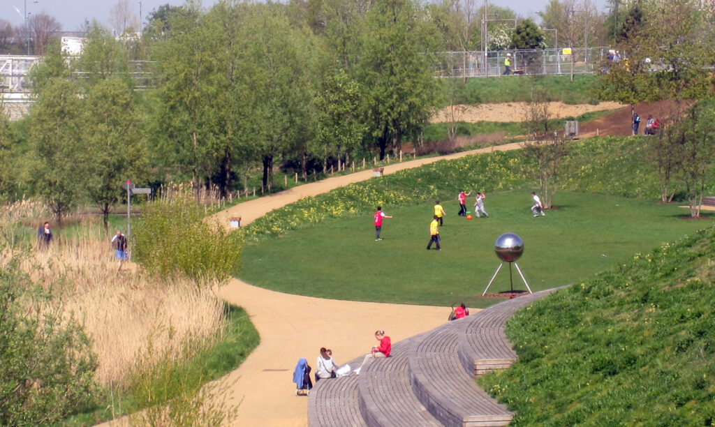 Looking down to path, meadow area, flat green space and trees, with people enjoying the spaces