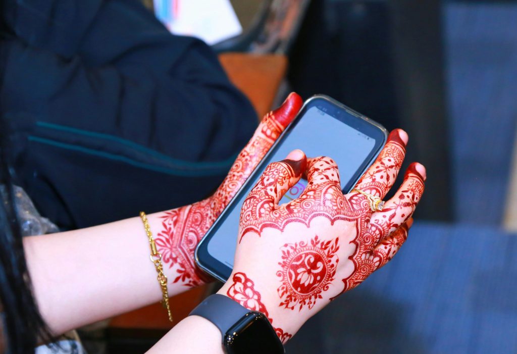 Hands with henna patterns, using a smartphone.