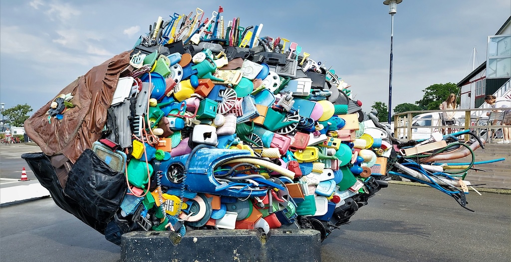 Esplanade with large fish sculpture, with a body made from colourful plastic beach debris.