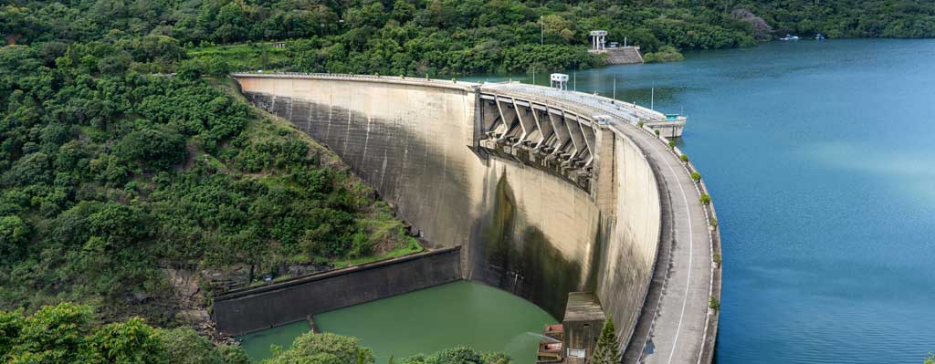 Hydroelectric dam, with blue reservoir to the right, and tress and valley to the left.