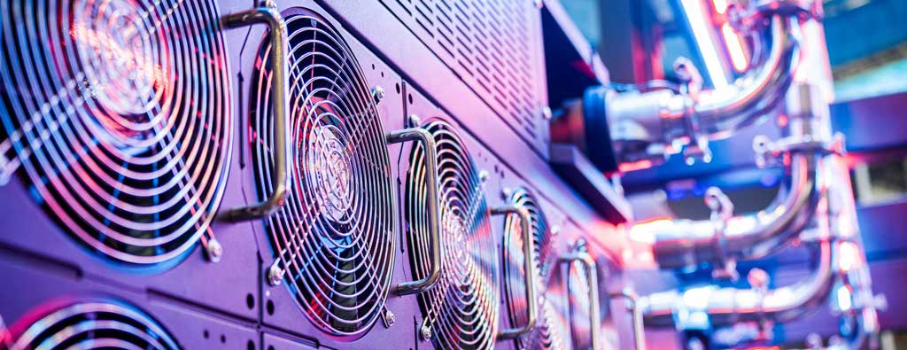 Fans and pipes as part of a computer server cooling system, bathed in a purple light.