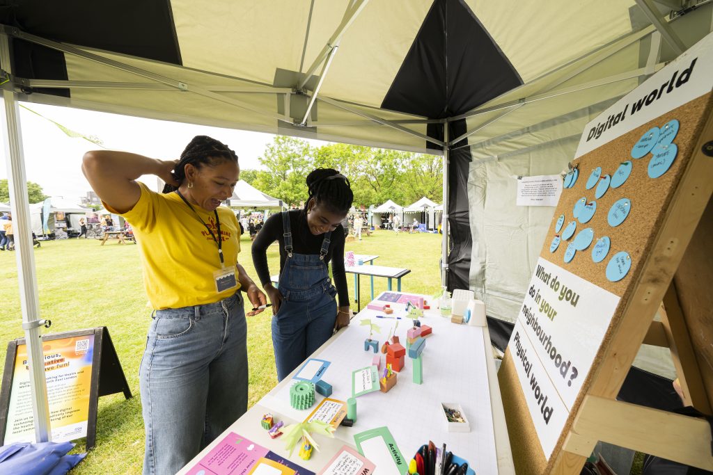 282_BIKE_FEST_220521_BF_ABK Two people looking at cards and objects on table and comments on a pin board